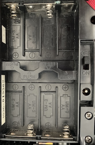 The battery bay of the Beetle, showing slots for eight AA batteries, a charge port, and an on/off switch.