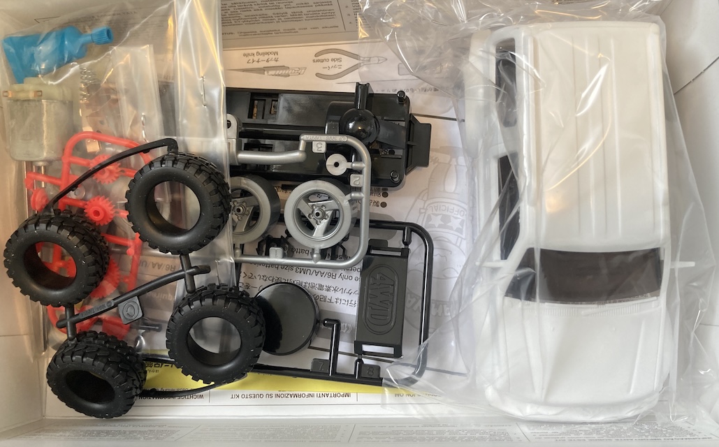 The box is opened, showing rubber tires, wheels, stickers, the body shell, and all the chassis parts.