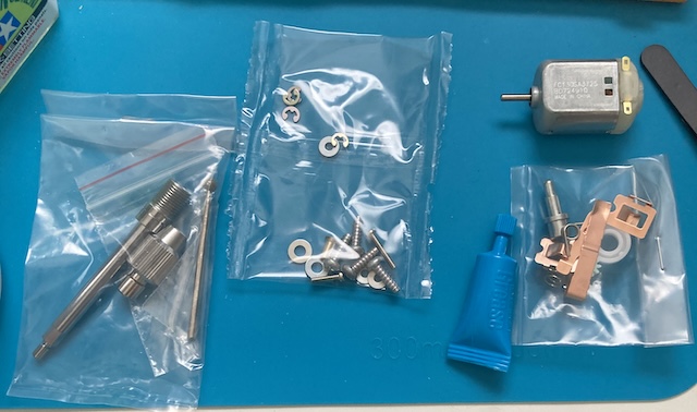 From left to right: a bag containing shafts, chucks, collets, and bits; another bag, containing e-clips, washers, and screws; and a third bag, containing a plastic 1150 bushing and battery terminals. There's also a made-in-China 130 motor and a tube of grease.